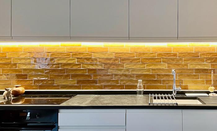 The kitchen has natural slate worktops, simple contemporary cupboards and brightly coloured tiled splash back.